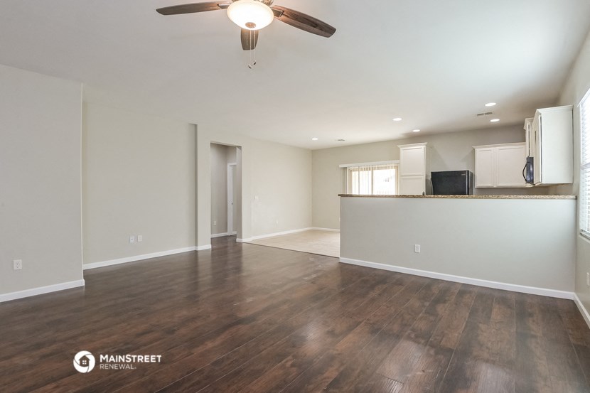 an empty living room with a ceiling fan and a kitchen