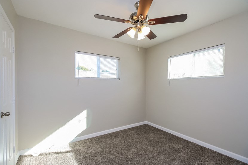 an empty room with a ceiling fan and two windows