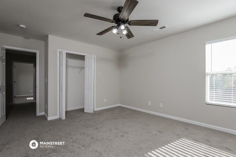 an empty living room with a ceiling fan and a closet