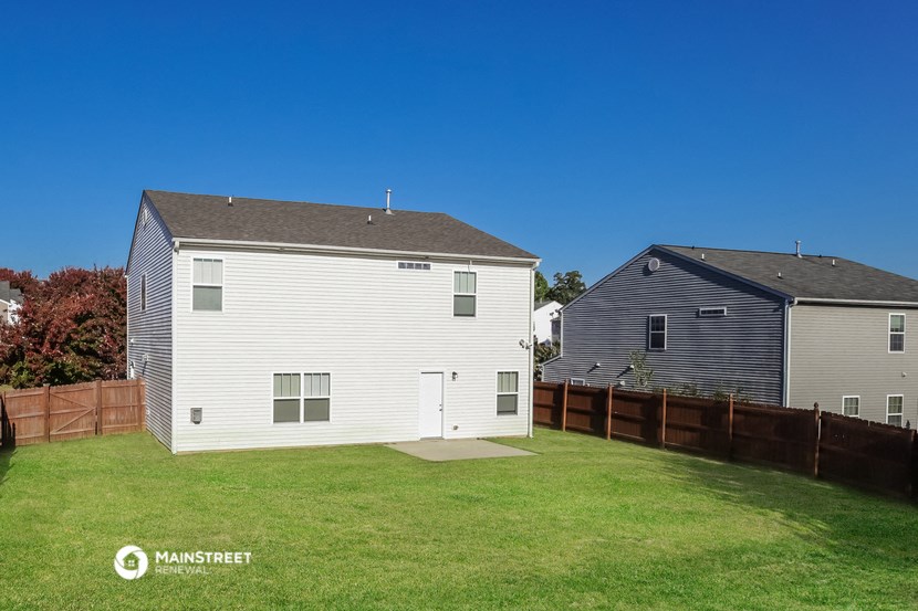 a backyard with a white house and a wooden fence