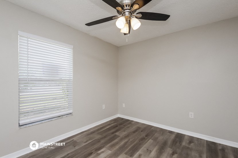 the spacious living room with a large window and a ceiling fan