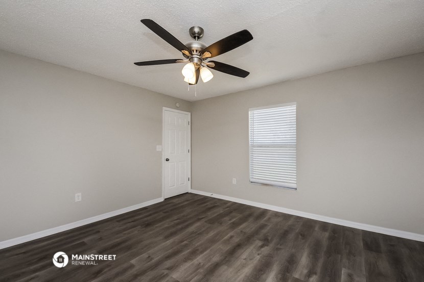 the spacious living room has a ceiling fan and hardwood floors