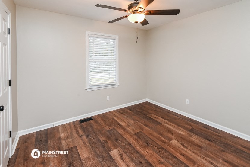 the spacious living room with hardwood flooring and a ceiling fan