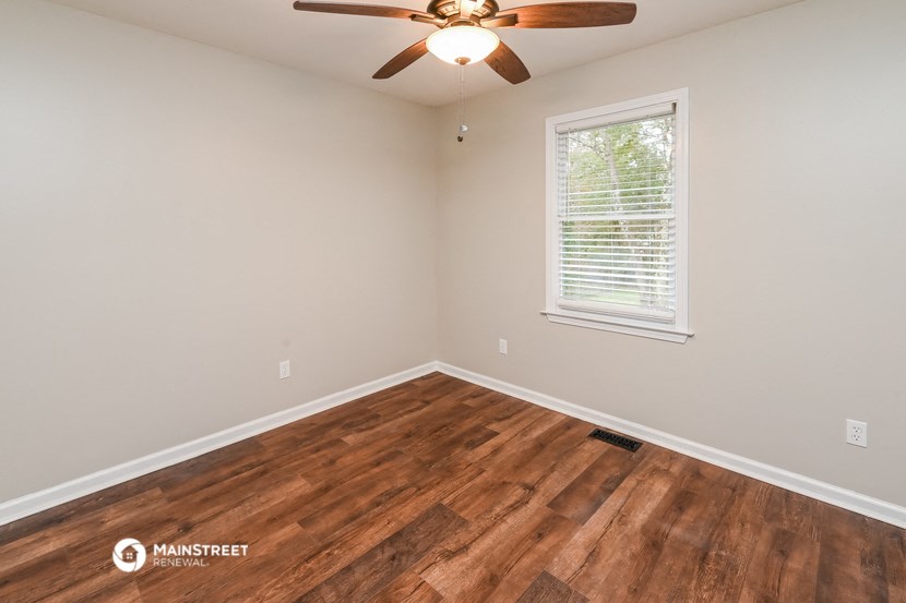 the spacious living room with hardwood floors and a ceiling fan