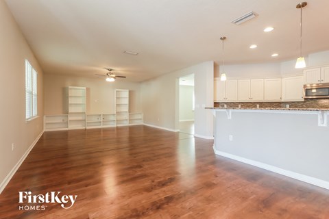 A spacious room with wooden floors and a kitchen area in the background.