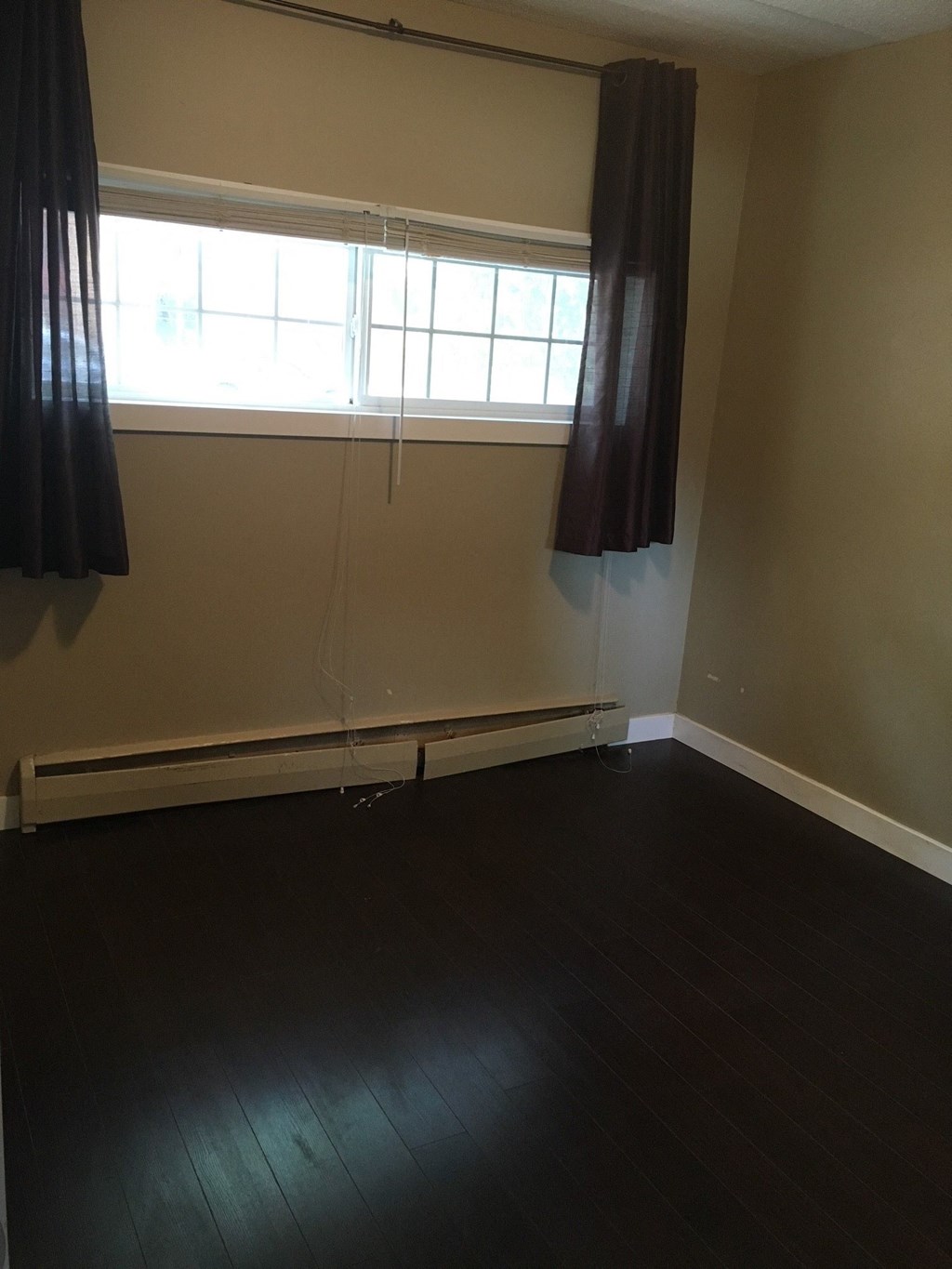 an empty room with dark wood floors and a window