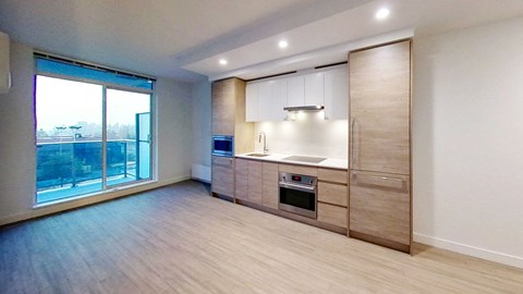 an empty living room with a kitchen and a large window