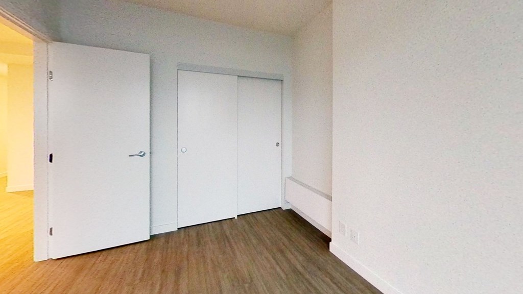 a bedroom with white walls and wooden floors and closets