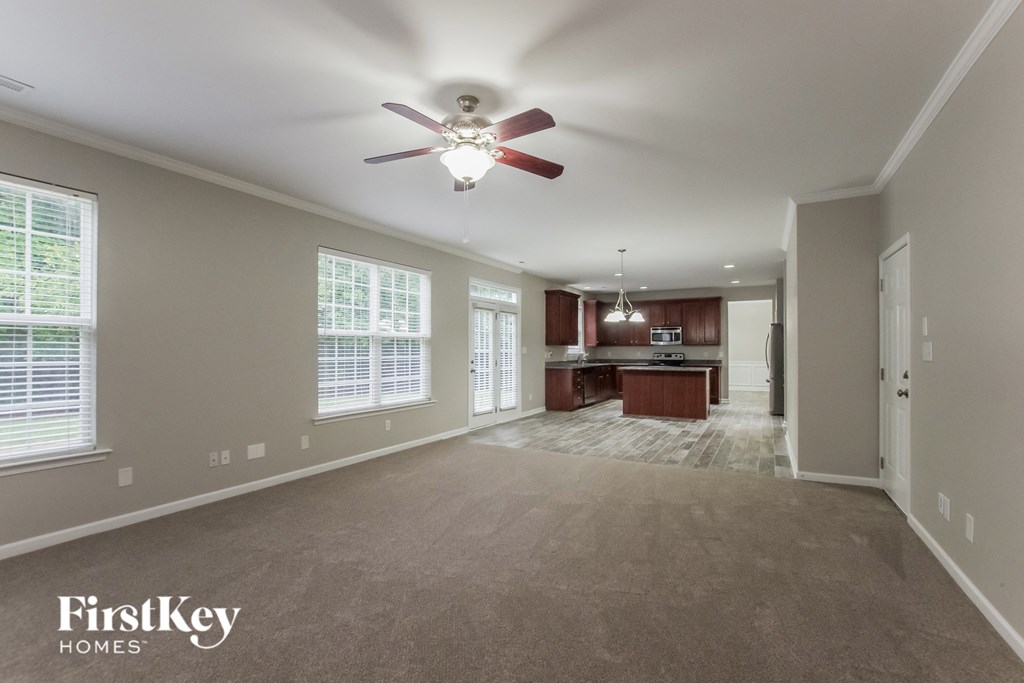 an empty living room with a ceiling fan and a kitchen