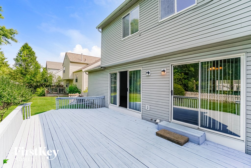 a white deck in front of a gray house with sliding glass doors