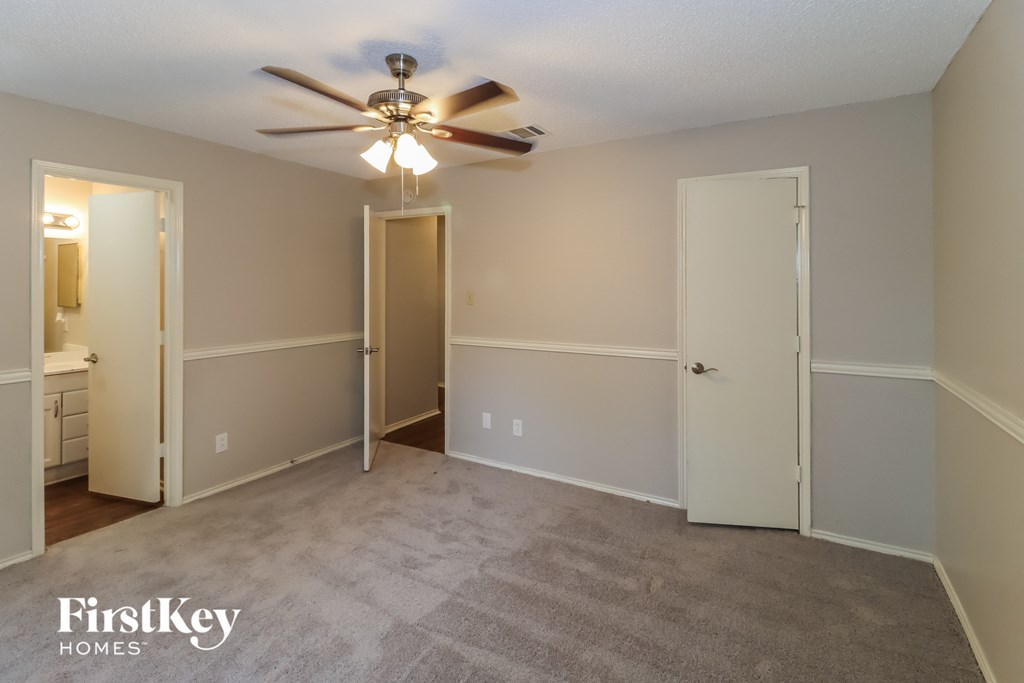 an empty living room with a ceiling fan and a door to a bathroom