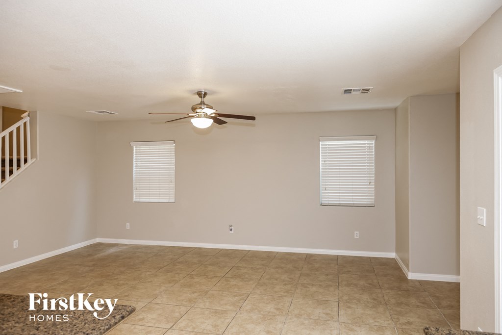 A spacious empty room with a ceiling fan and tiled floor.