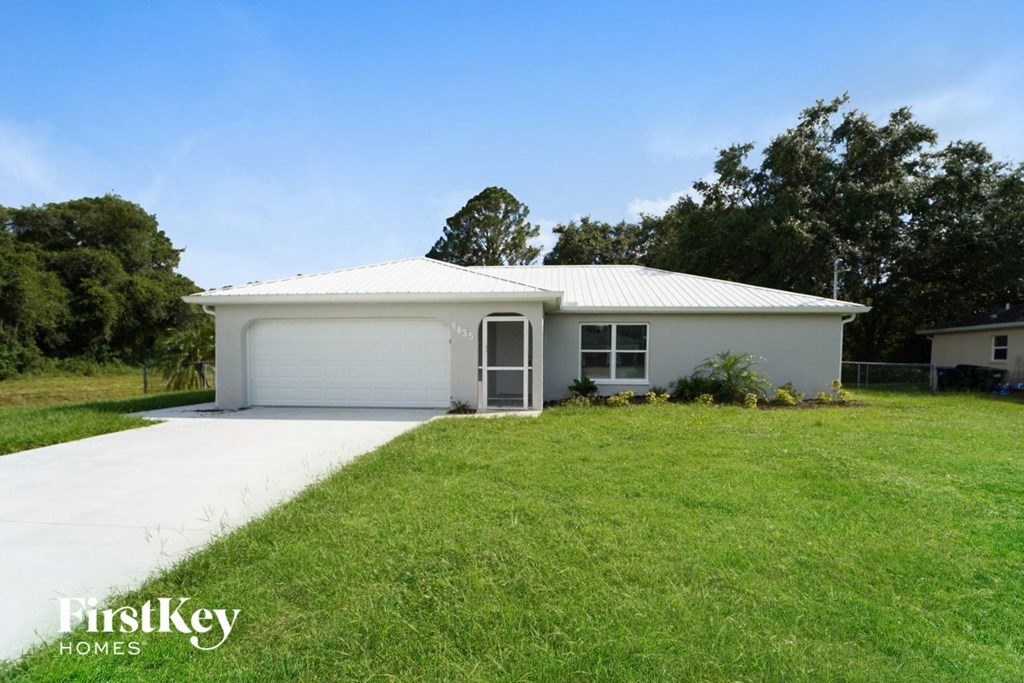 A white house with a garage door is surrounded by green grass.