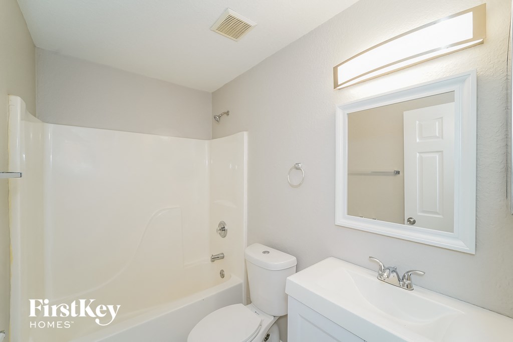 A white bathroom with a toilet, sink and mirror.
