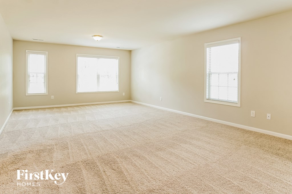 A sparsely furnished room with a carpeted floor and two windows.