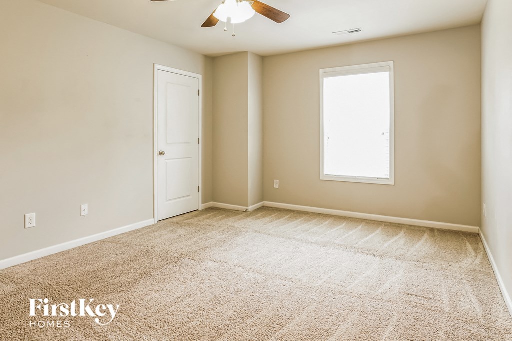 A room with a carpeted floor, a ceiling fan, and a window.