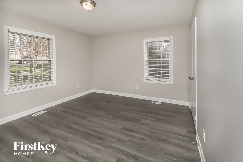a bedroom with wood flooring and two windows