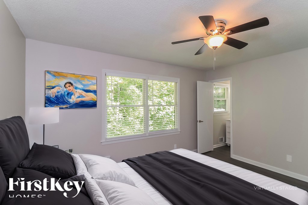 A bedroom with a bed, a ceiling fan, and a painting on the wall.