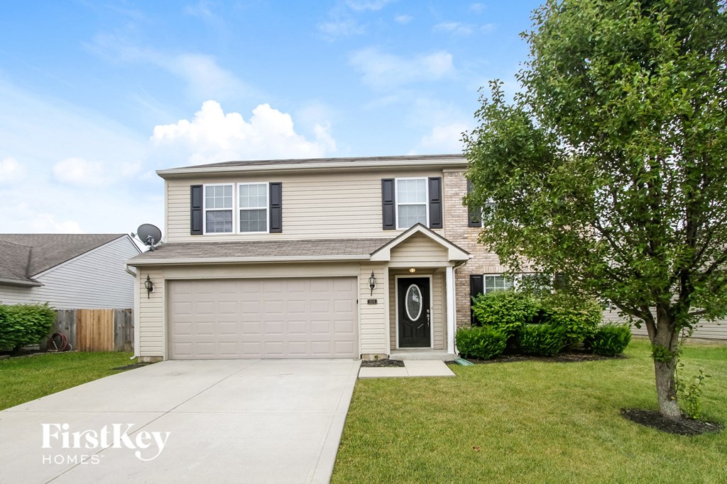 A house with a garage and a tree in front of it.