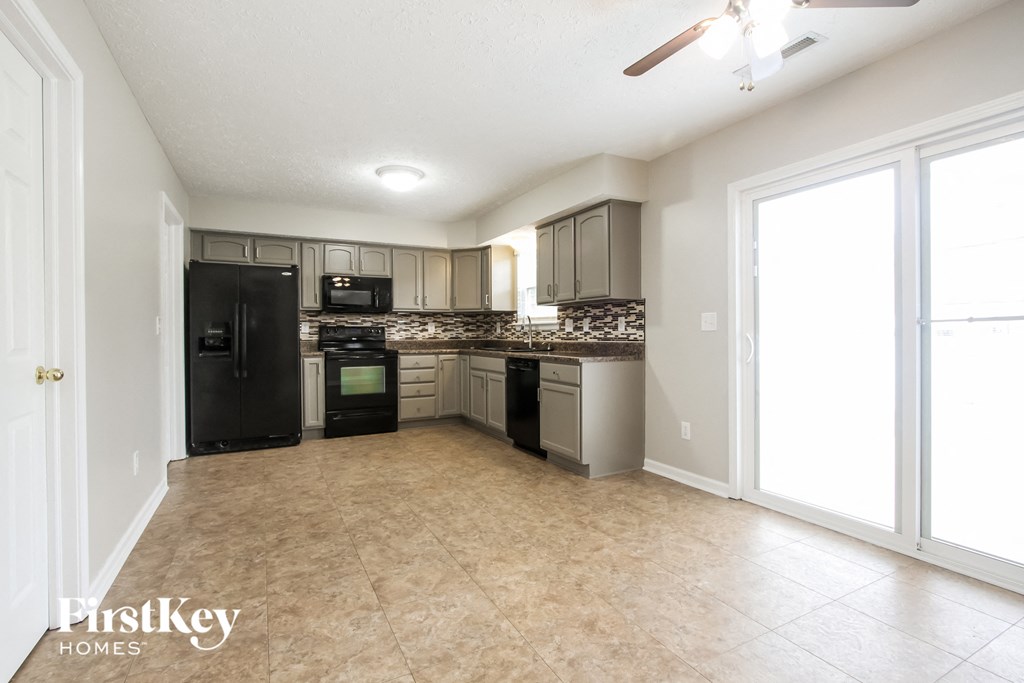 A kitchen with a black refrigerator, microwave, and oven with a tile backsplash and a tile floor.