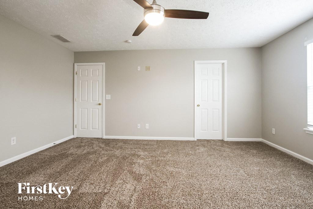 A room with a carpeted floor and a ceiling fan.