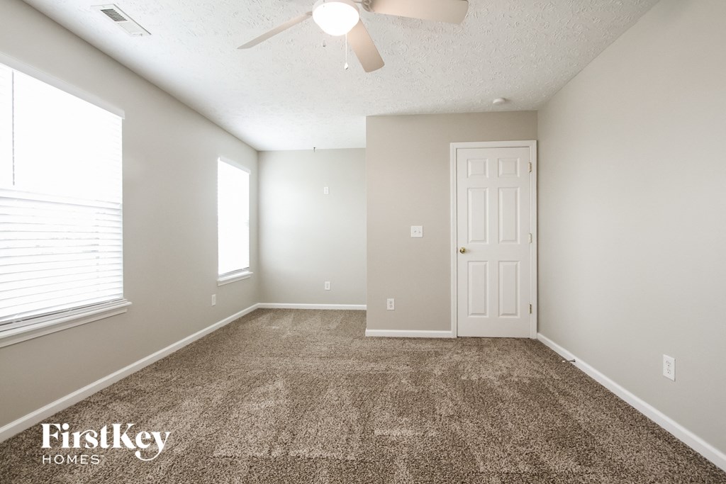 A room with a carpet floor, a ceiling fan, and a door.