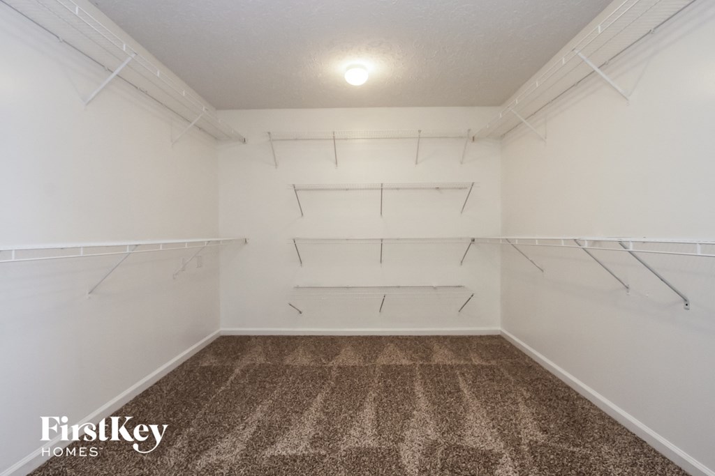 A white empty room with a carpet floor and a FirstKey HOMES logo.