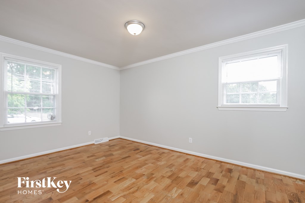 a bedroom with a hardwood floor and two windows