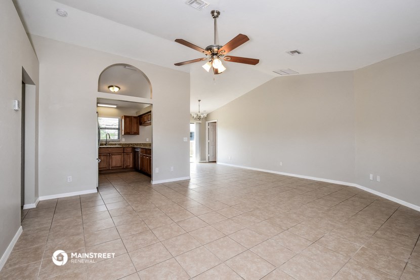 an empty living room with a ceiling fan and a kitchen