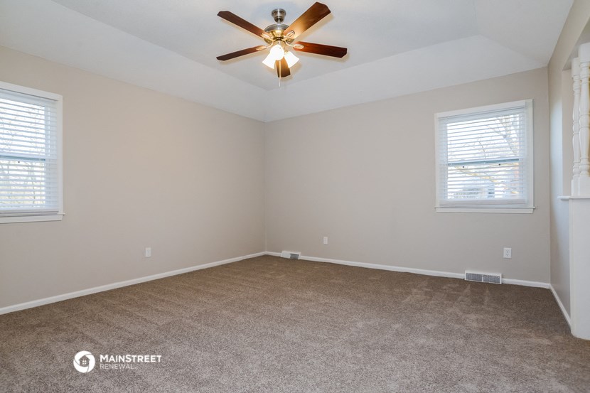 the spacious living room with ceiling fan and carpet