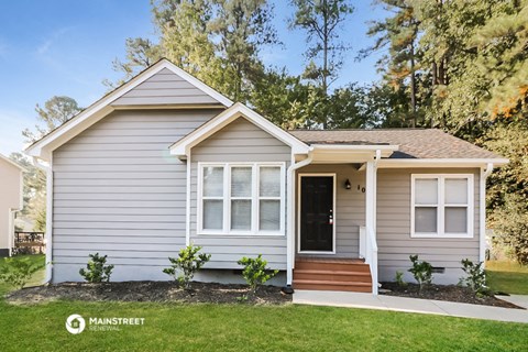 a small gray house with a lawn and trees