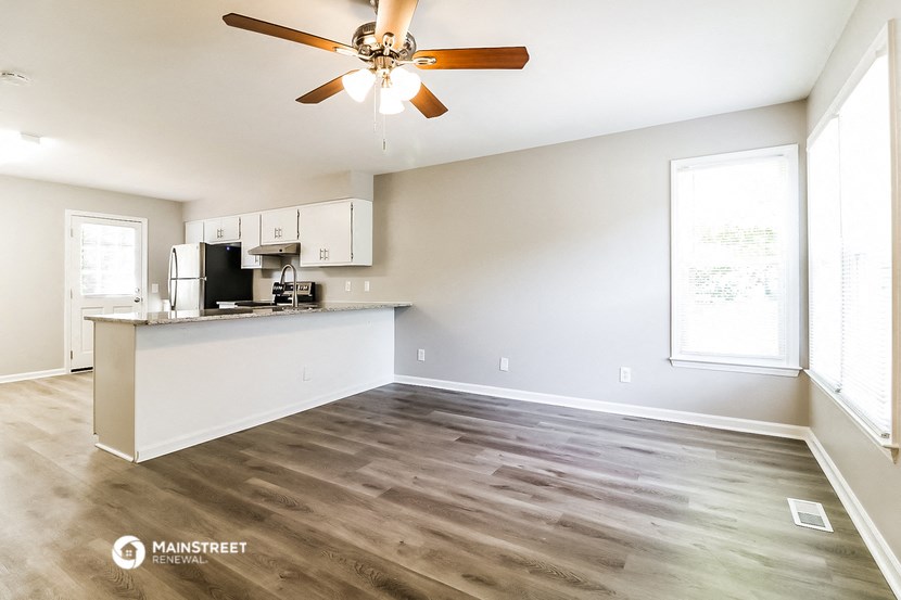 an empty living room with a kitchen and a ceiling fan