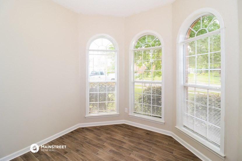 a living room with three windows and a wooden floor