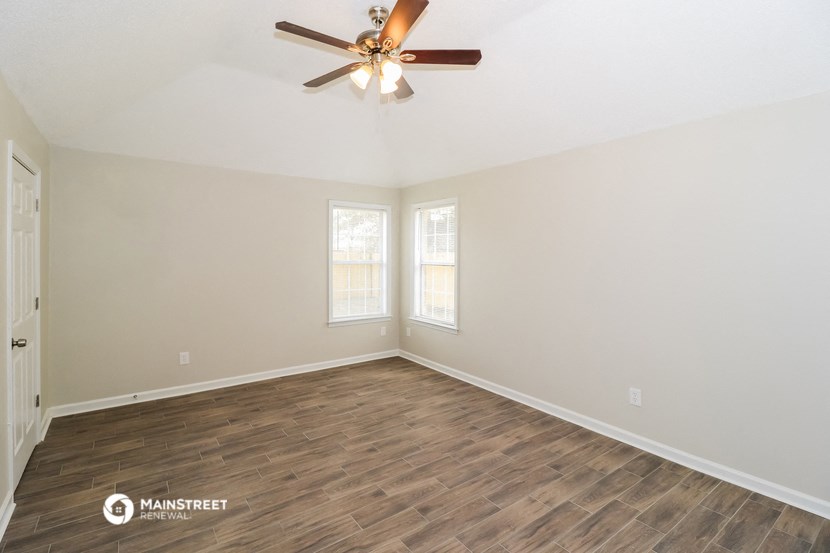 the spacious living room with wood flooring and a ceiling fan