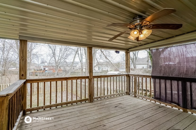 a covered deck with a ceiling fan and large windows