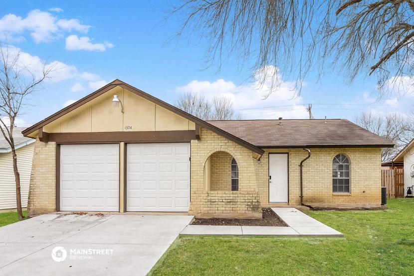 a tan brick home with white garage doors and a lawn