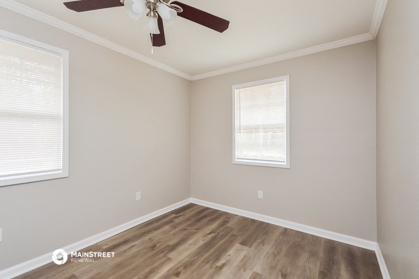 an empty room with a ceiling fan and two windows