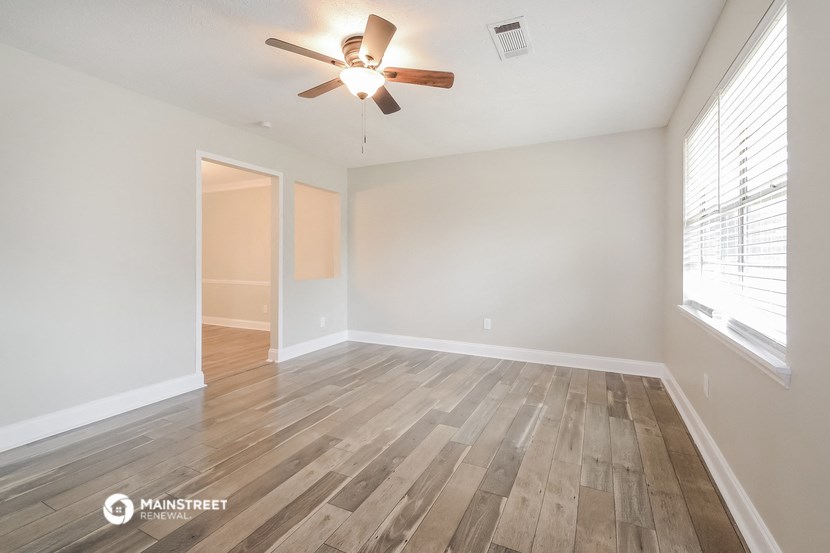 the spacious living room with wood flooring and a ceiling fan