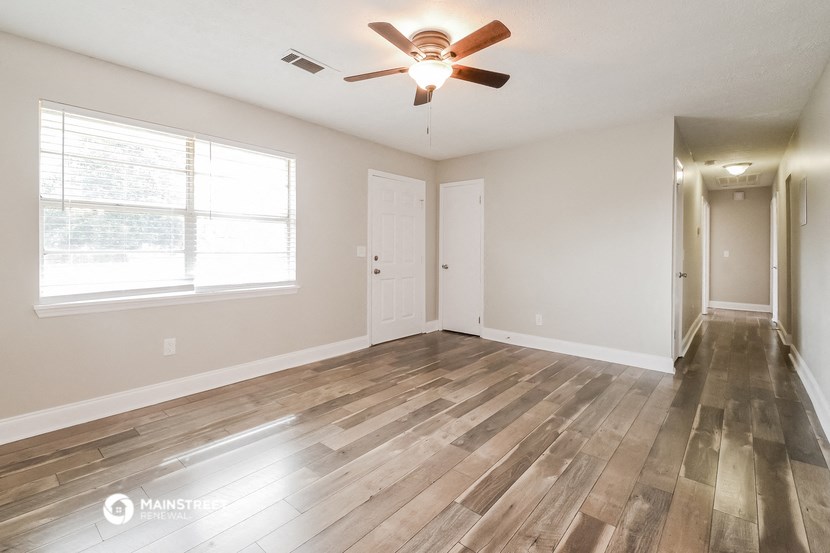 the spacious living room with hardwood floors and a ceiling fan