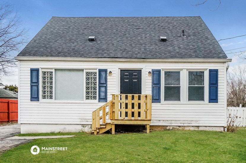 the front of a white house with a blue door and a wooden deck