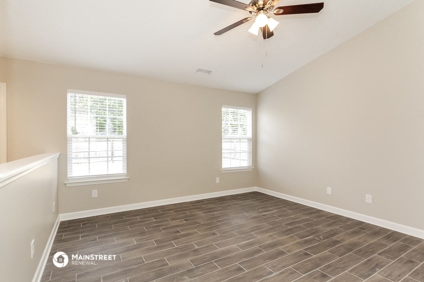 the spacious living room with wood flooring and a ceiling fan