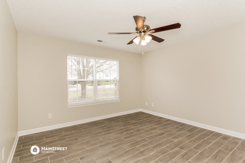 the spacious living room with a ceiling fan and a window
