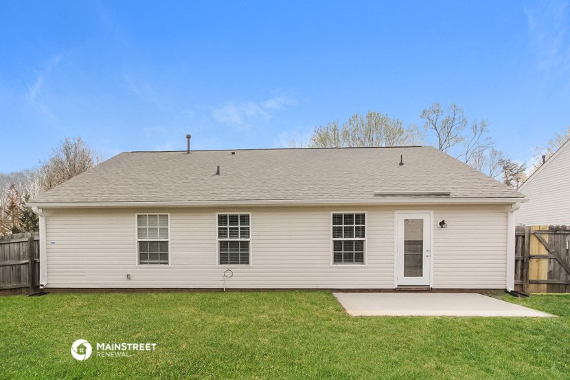 the front of a white house with a yard and a wooden fence