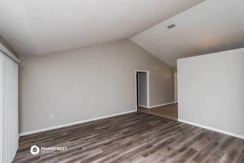 the living room of an apartment with wood flooring and white walls