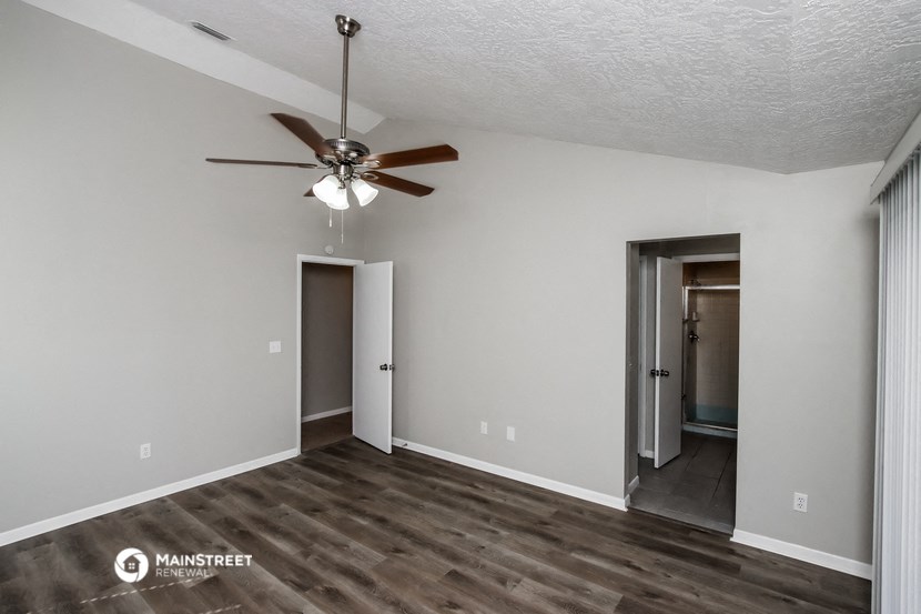 an empty living room with a ceiling fan and a door to a hallway