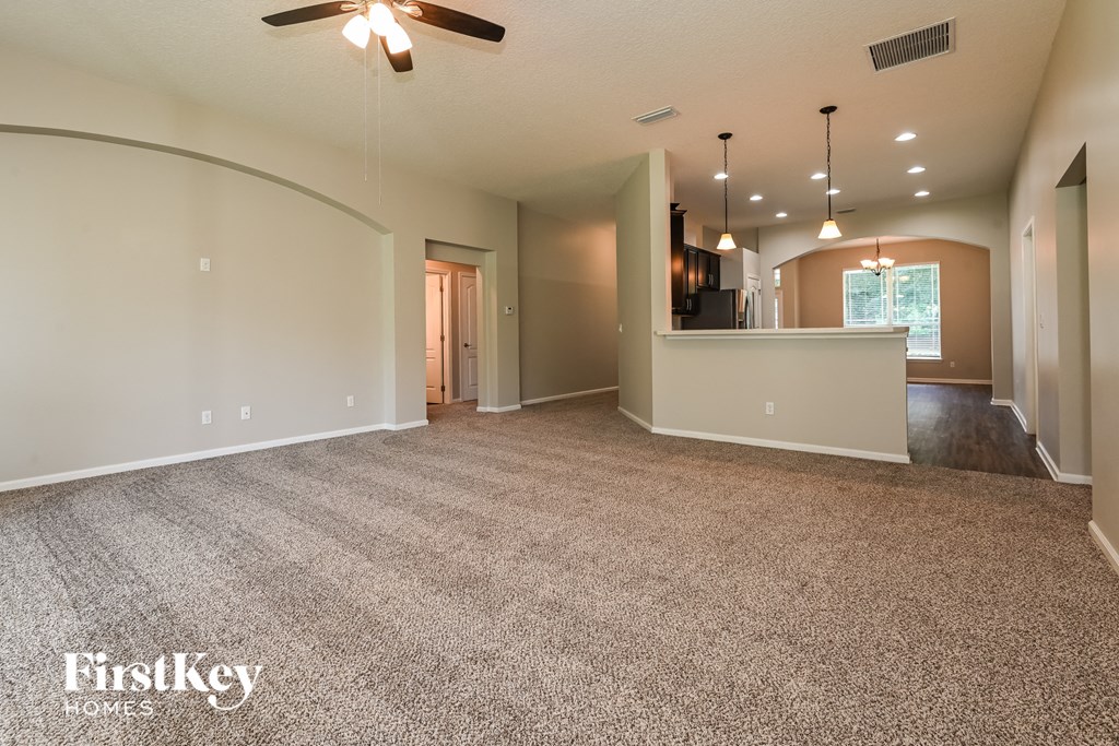 an empty living room with a kitchen and a ceiling fan