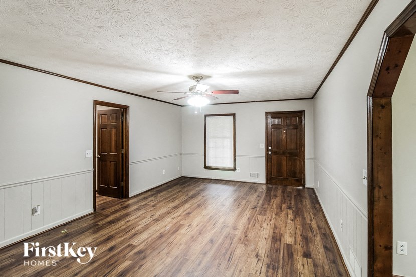 A room with wooden floors and white walls, with a ceiling fan and two doors.