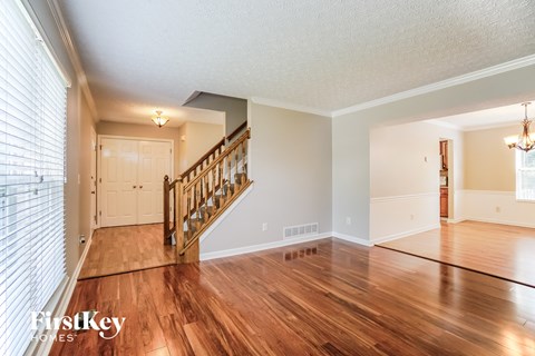 the living room and entryway of a house with wood floors and a staircase