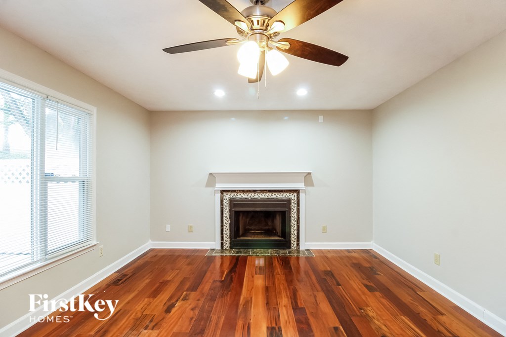 a living room with a fireplace and wooden floors and a ceiling fan