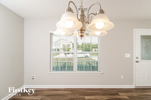 A chandelier hangs over a window in a room with a wooden floor.